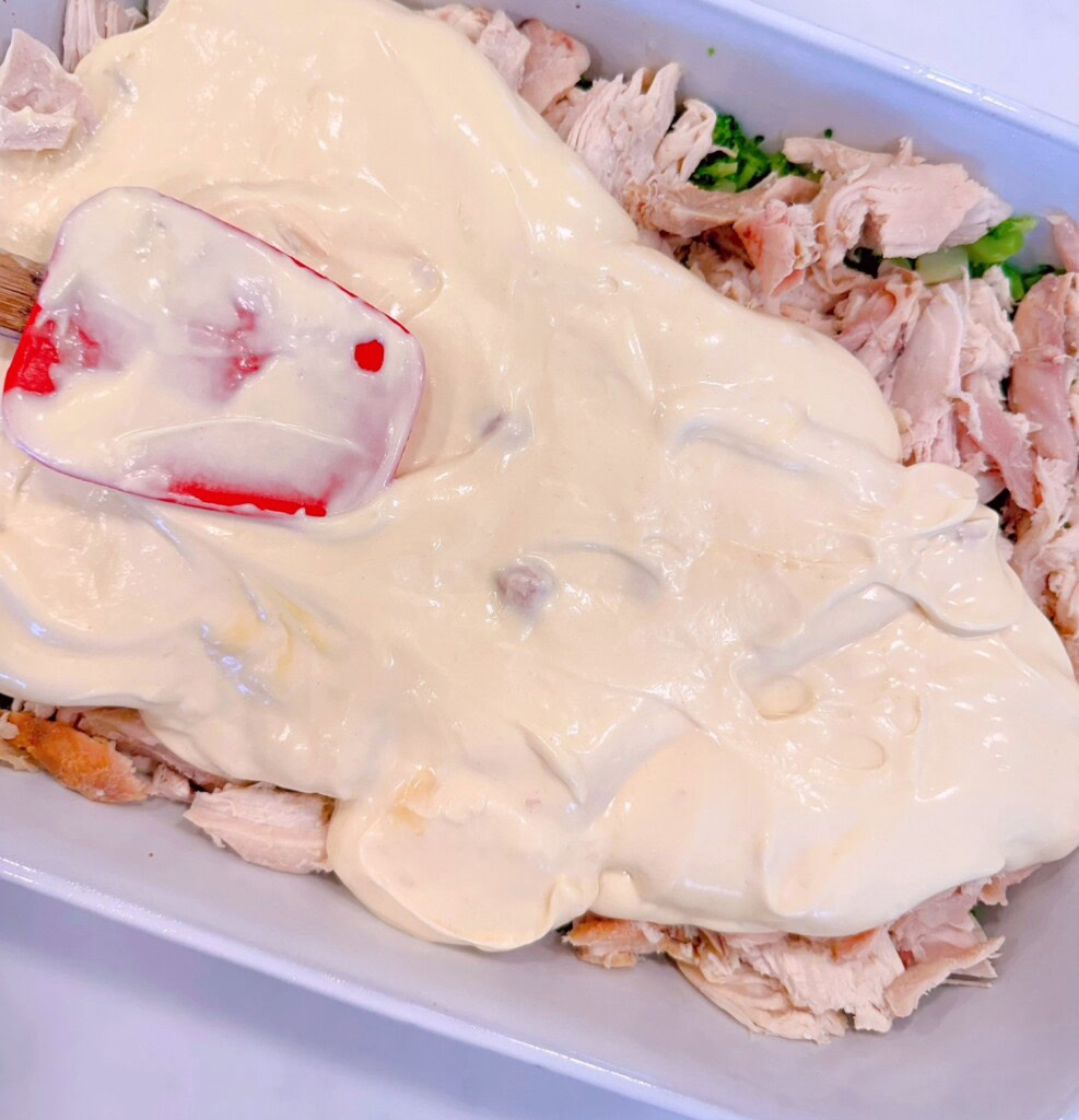 Spreading cream sauce over chicken and broccoli in casserole dish.