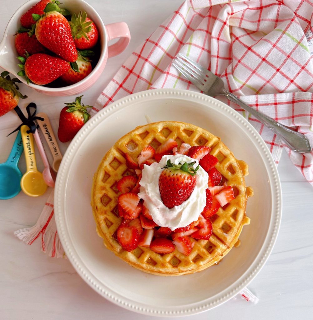 Overhead shot of Strawberry Vanilla Waffles with fresh strawberries, whipped cream on a white plate.