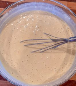 Mixed waffle batter in a glass bowl with wire whisk.