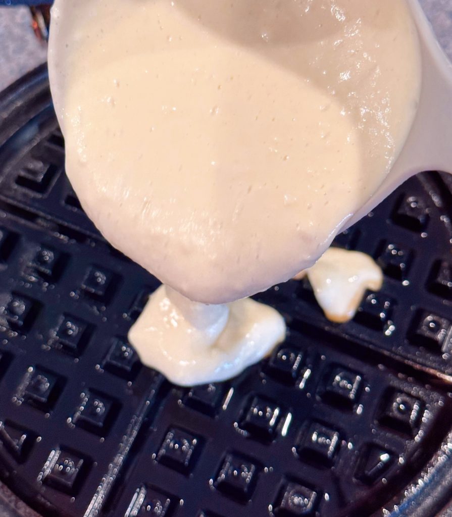 Pouring waffle batter on a hot waffle iron.