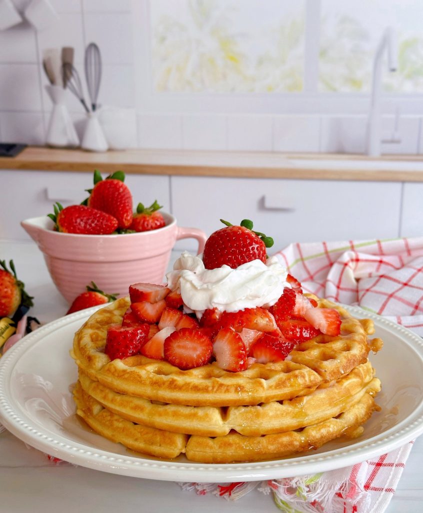 Stack of waffles with fresh strawberries on top and whipped cream. 