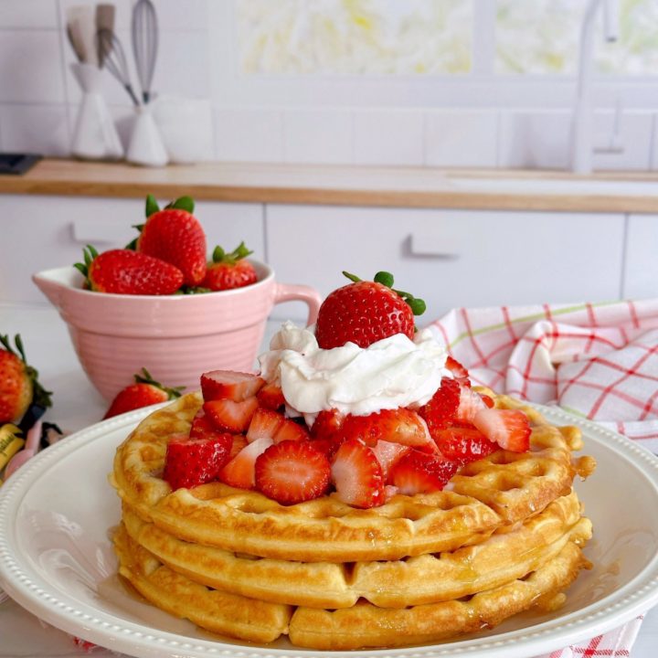 Stack of waffles with fresh strawberries on top and whipped cream.