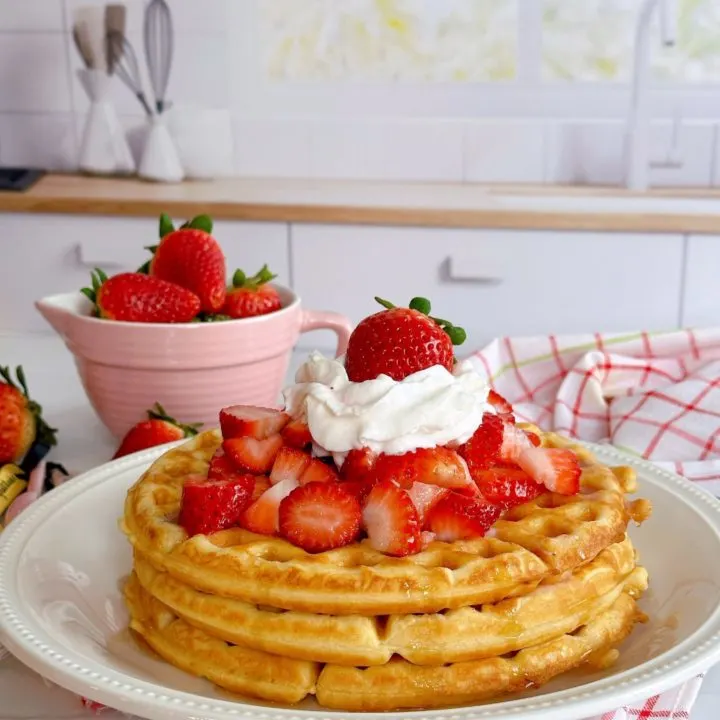 Stack of waffles with fresh strawberries on top and whipped cream.