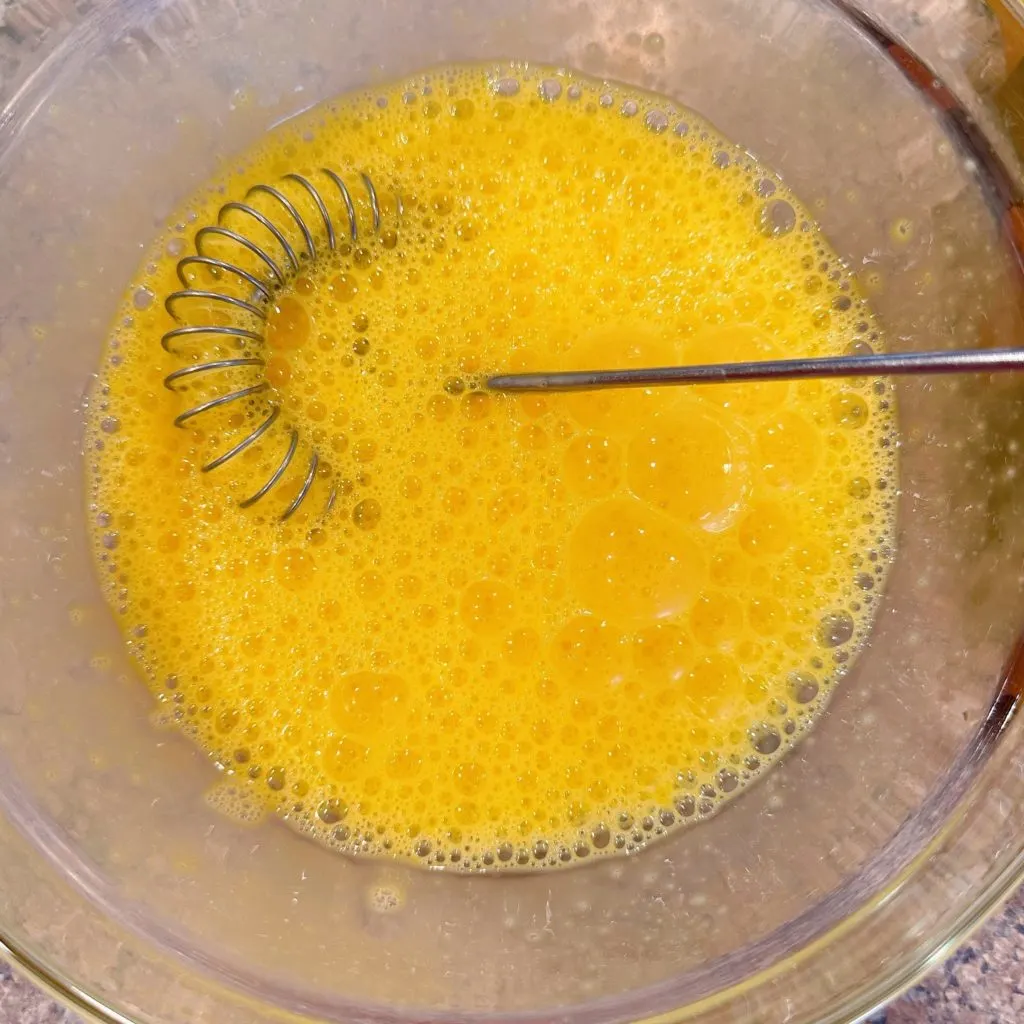 Whipped eggs in a bowl with wire whisk.