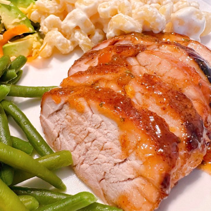 Sliced Pork Tenderloin on a plate with green beans and pasta alfredo.