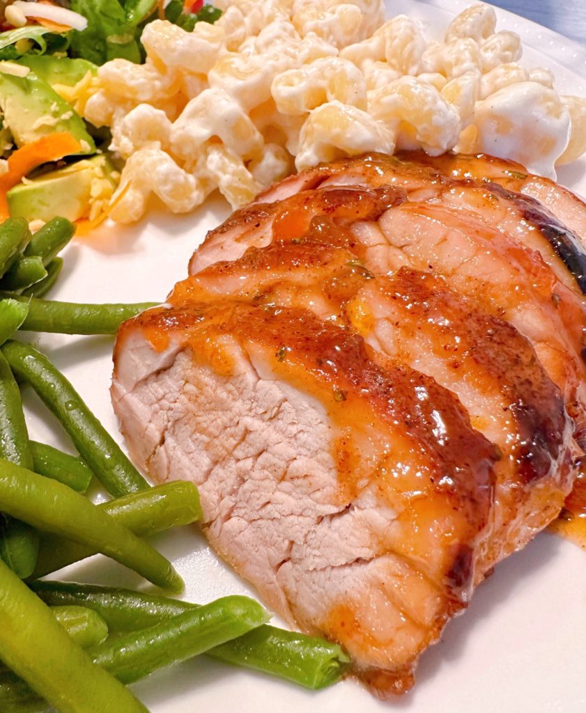 Sliced Pork Tenderloin on a plate with green beans and pasta alfredo.