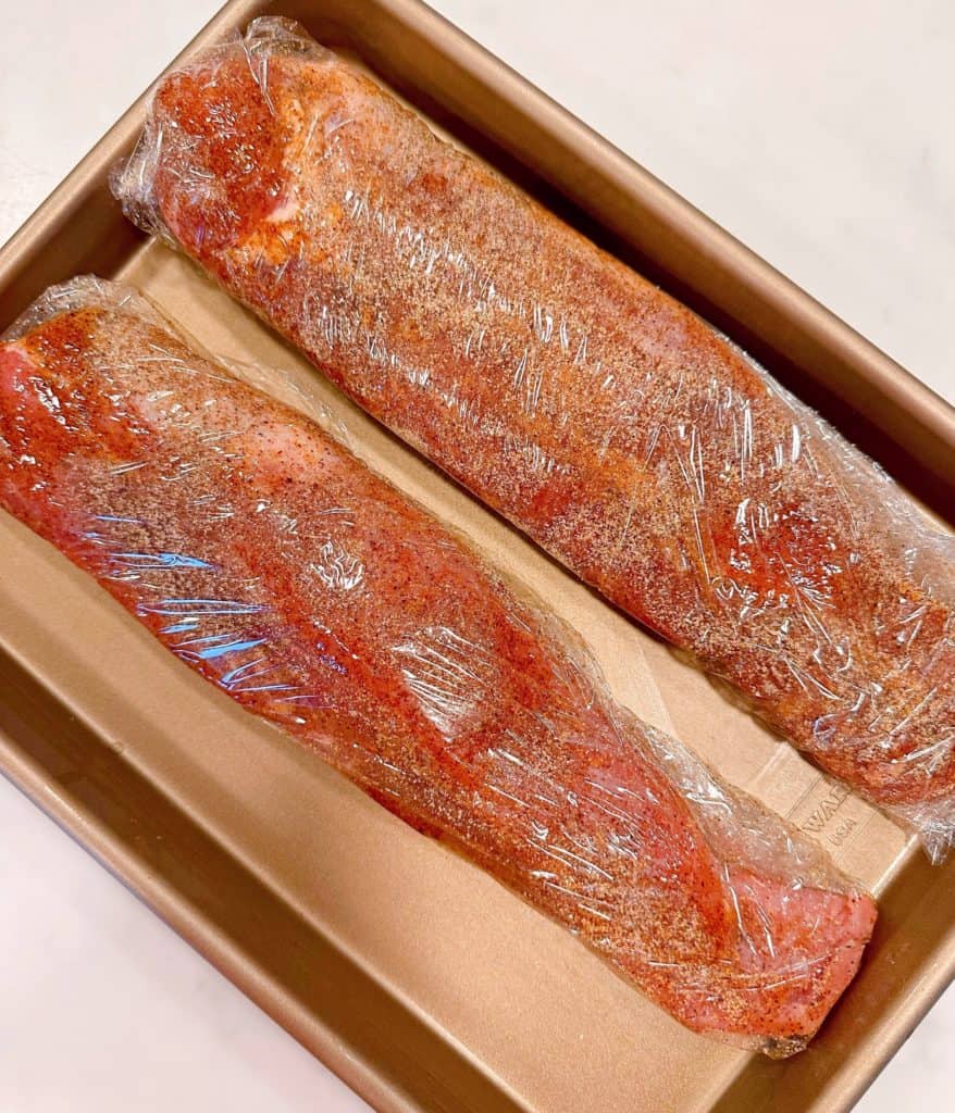 Pork tenderloins seasoned and wrapped in plastic wrap.