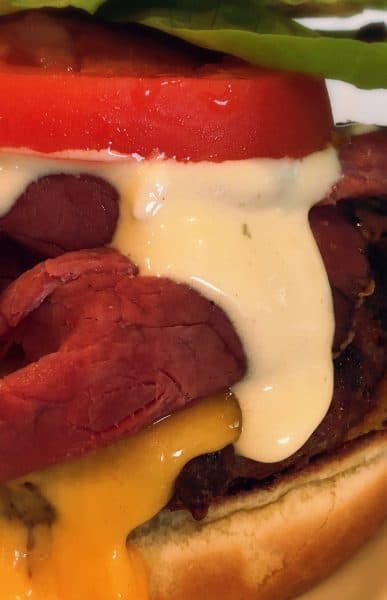 Thick Declicious Pastrami Burger with melted cheddar cheese, sliced tomatoes, spinach leaves and a heafty dose of Dijon Blue Cheese Sauce