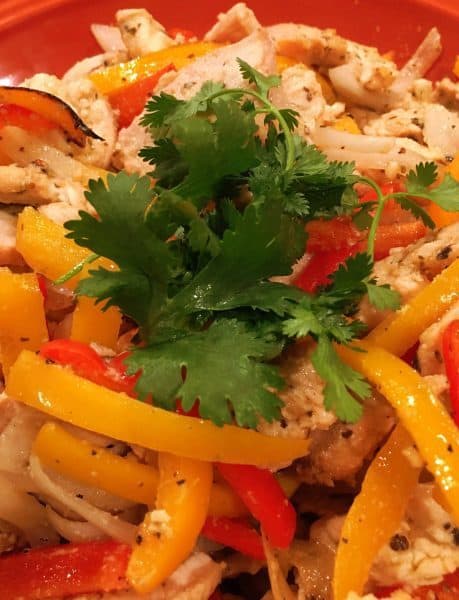 Large bowl filled with grilled chicken and peppers with fajita seasonings topped with a sprig of fresh cilantro. Tangy Chicken Fajitas are ready for tortillas.