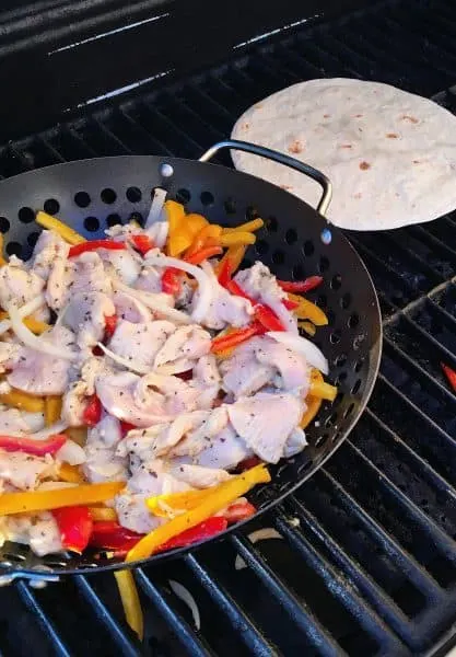 Grilling Chicken and Pepper Fajita Mix on BBQ in a grilling basket. Next to the grilling basket flour tortillas are being roasted.