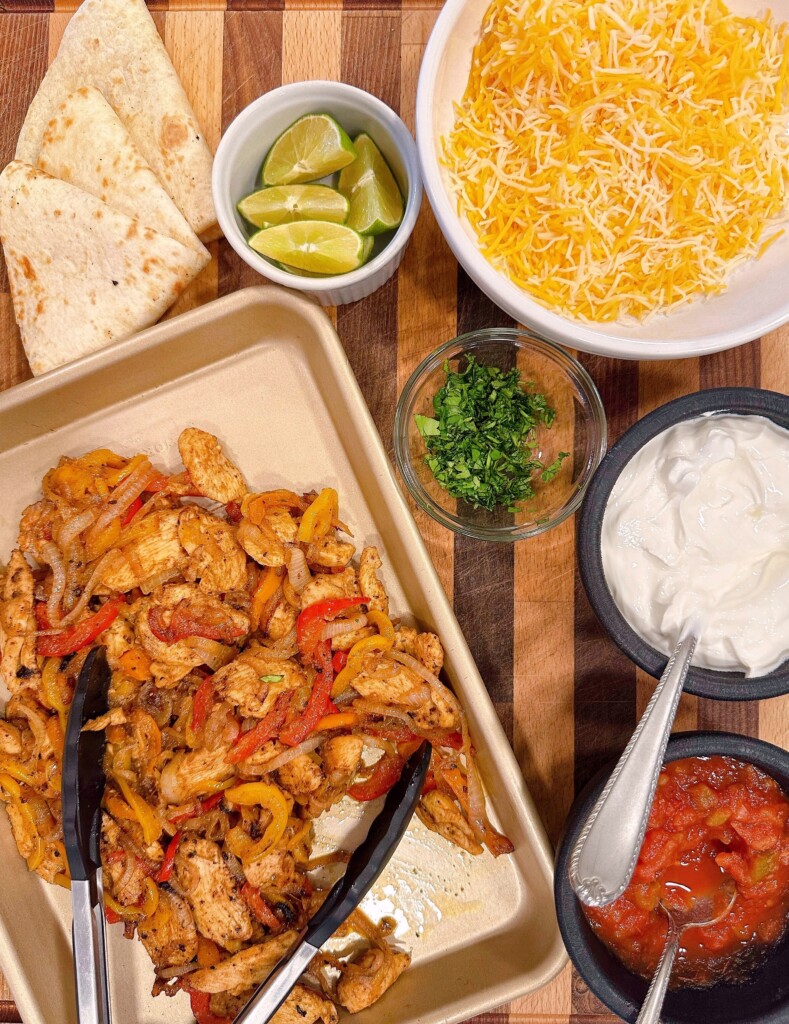 Chicken fajitas and toppings on a cutting board ready to assemble.