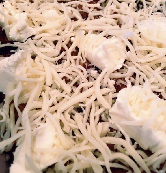 Layer of ricotta cheese and grated cheese on top of eggplant for eggplant parmigiana.