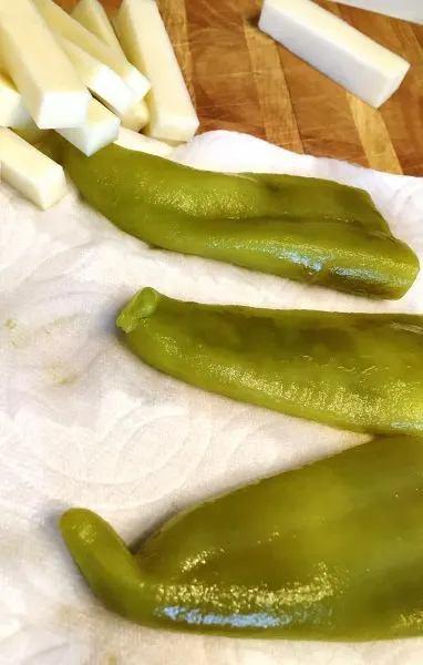 Canned chili peppers draining on a paper towel next to chunks of Jack Cheese.