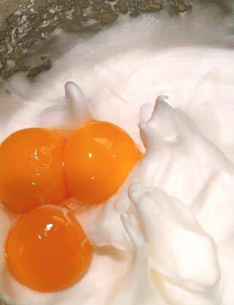 Egg whites beaten to stiff peaks with three egg yolks waiting to be folded into egg whites.