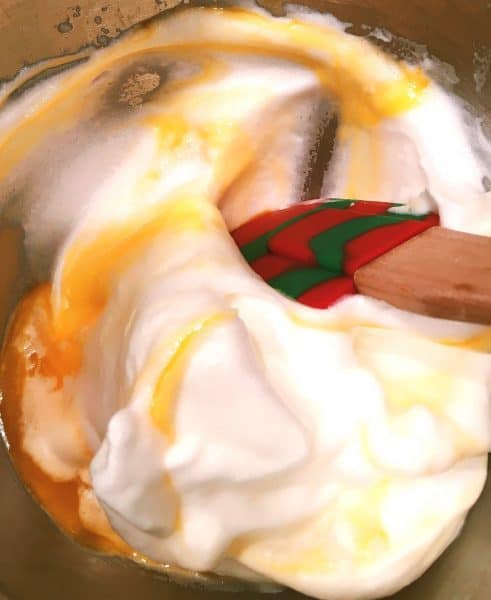 Folding in the egg yolks into the beaten egg whites with a spatula.