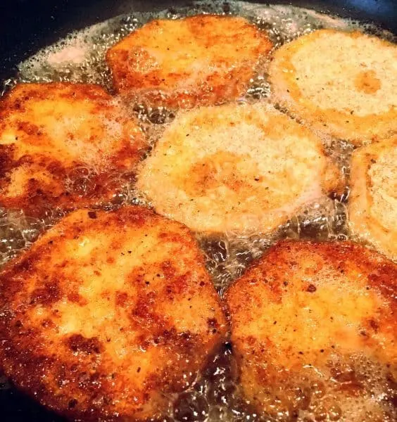 Skillet with hot oil and breaded eggplant frying in pan to a golden brown