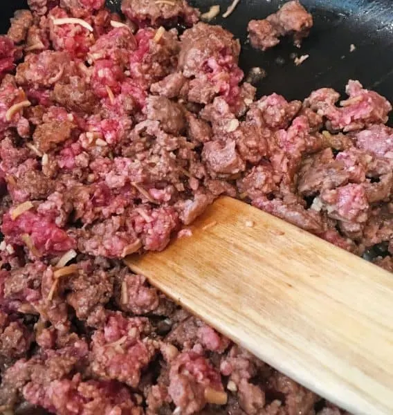 Hamburger meat with dried onion flakes in a skillet being browned over high heat.