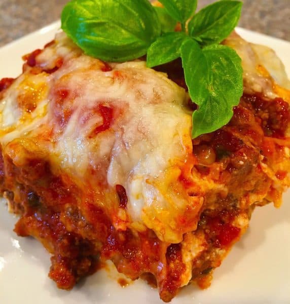 Slice of eggplant of parmigiana on a white plate and topped with basil