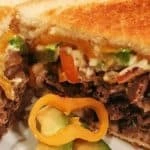 Two slices of toasted bread with roast beef, cheese, peppers and tomatos in between