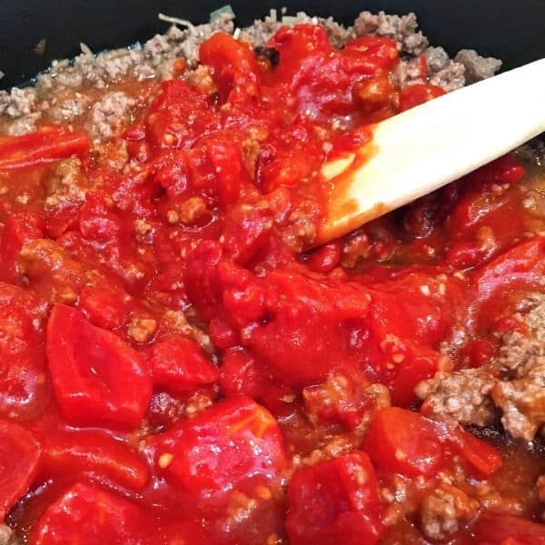 Adding tomatoes to meat to create meat sauce of Eggplant Parmigiana