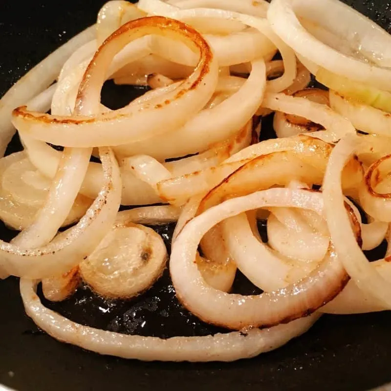 Hot skillet filled with thinly sliced onions that have been caramelized.