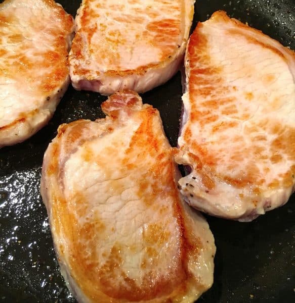 Pork Chops being browned in a skillet with olive oil.