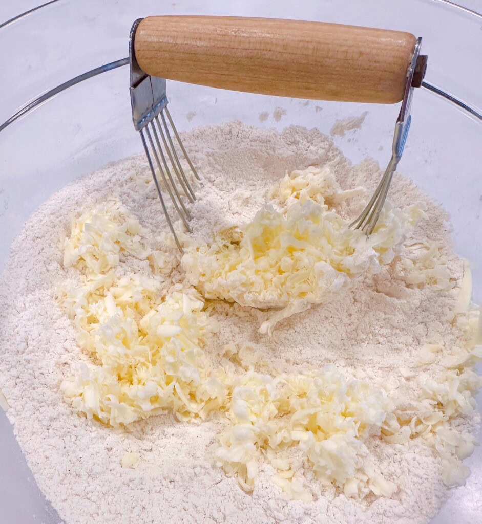Grated frozen butter being "cut" into dry ingredients with a pastry cutter.