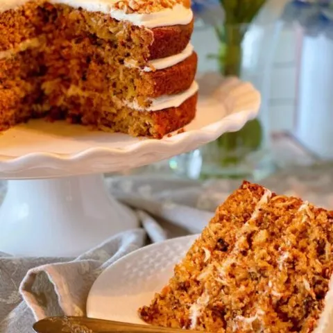 World's best carrot cake on cake stand with a slice on a plate in front