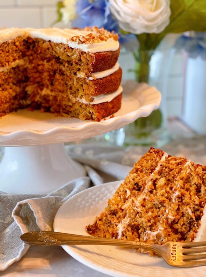 World's best carrot cake on cake stand with a slice on a plate in front