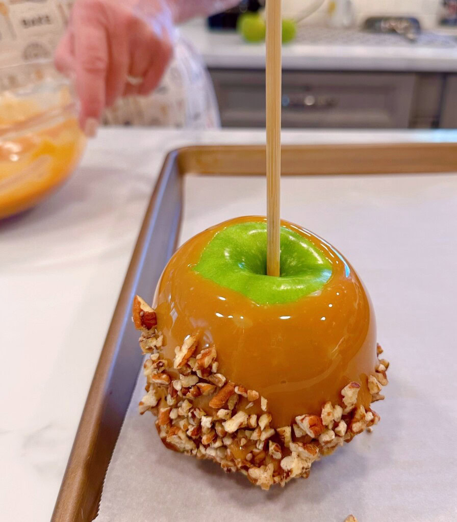 Dipped apple with nuts on parchment lined baking sheet.