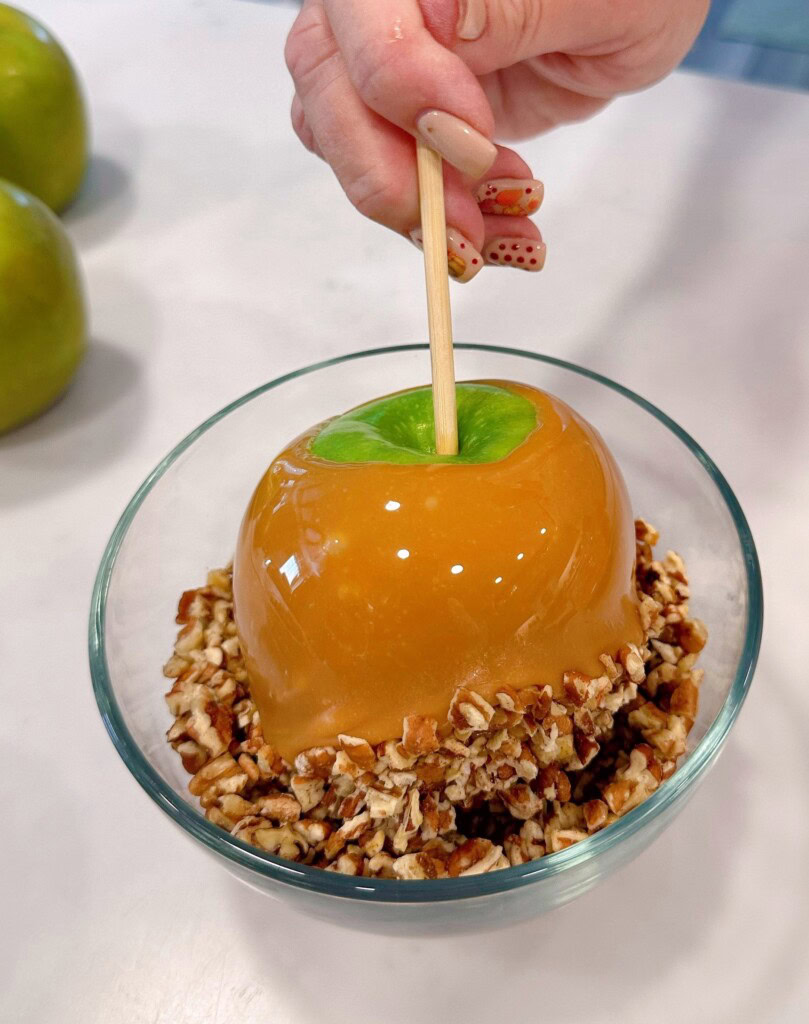 Dipping the caramel apple in the chopped nuts.