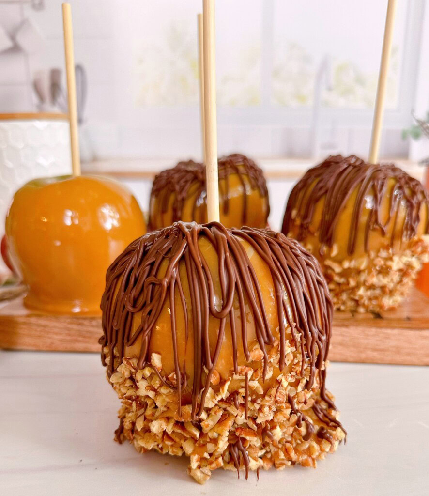 Double Caramel Apples with nuts and chocolate on a table top.