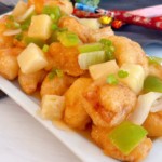 Sweet and Sour Chicken on a white platter with onion, green peppers, and pineapple.