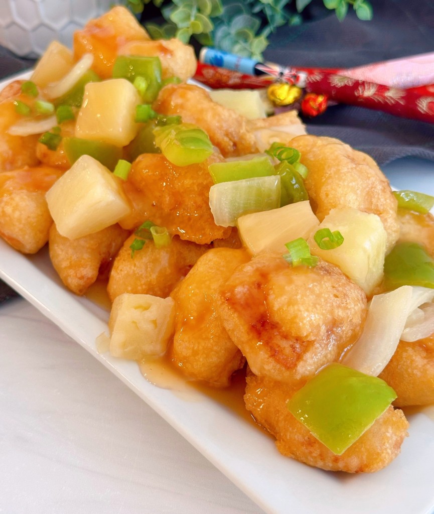 Sweet and Sour Chicken on a white platter with onion, green peppers, and pineapple.