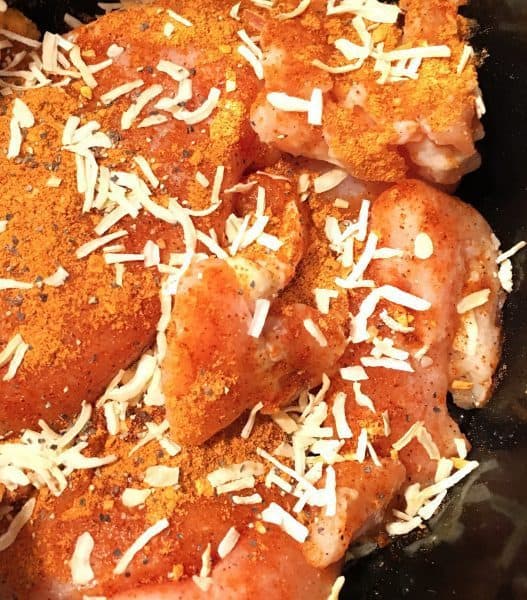 Chicken breasts layered in a slow cooker with onion flakes, and taco seasonings