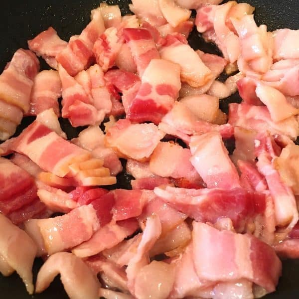 cut bacon in large skillet cooking on hot stove top