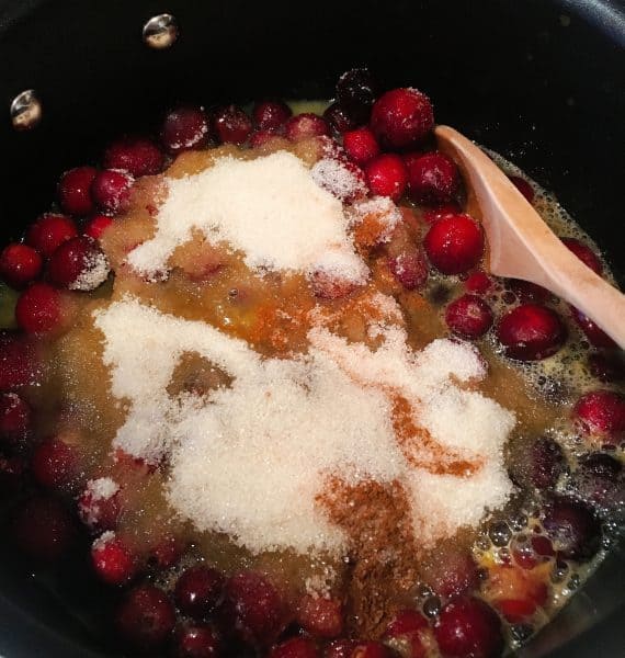 Cranberries, sugar, and orange juice with spices in a sauce pan over heat.