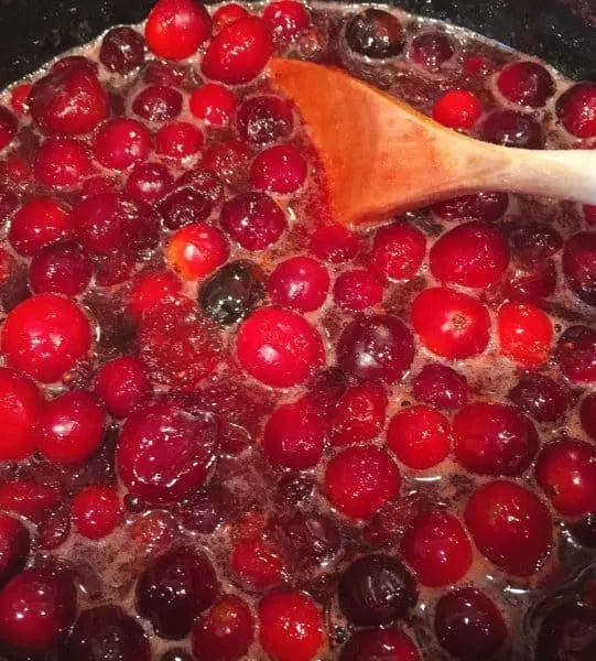 Cranberries in orange juice boiling on the stove.