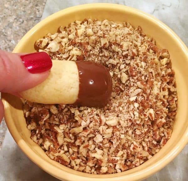 Rolling chocolate dipped orange logs into chopped pecans
