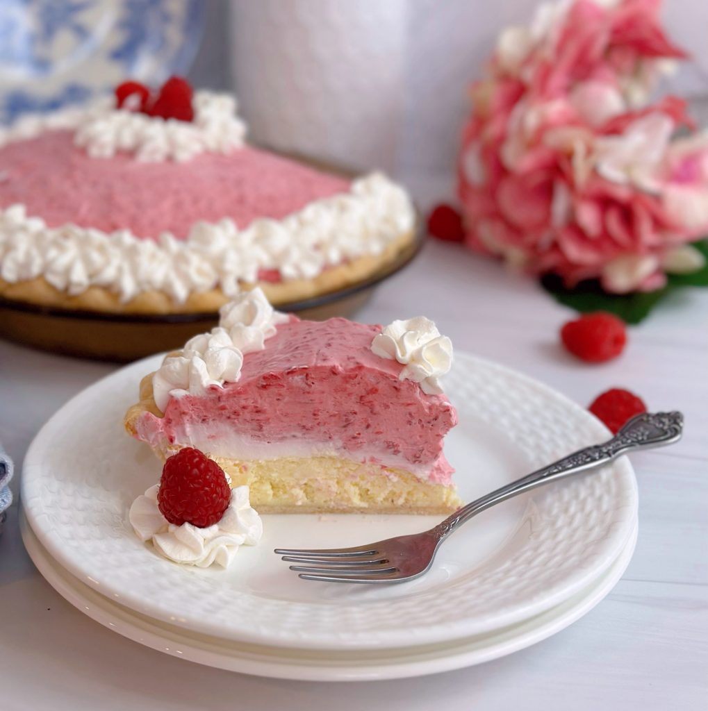 Raspberry Cream Pie with a slice on a white plate and the whole pie in the background.