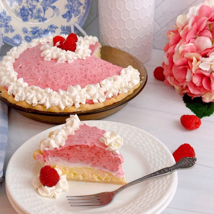 Raspberry Cream Pie with a slice on a dessert plate and the whole pie in the background.
