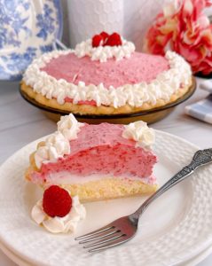 Raspberry Cream Pie Slice on a white plate with a fork and whole pie in the background.
