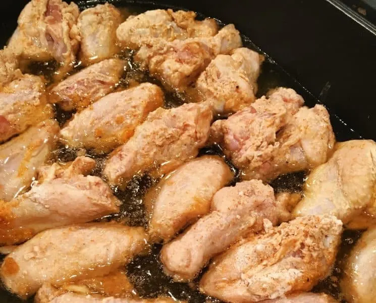 Coated wings in an electric skillet frying in oil until crispy