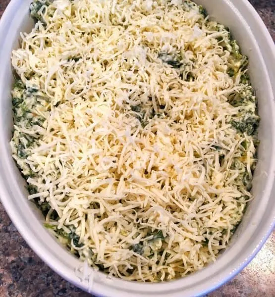 Small casserole dish with Spinach Artichoke dip and topped with grated Parmesan cheese ready to go into the oven
