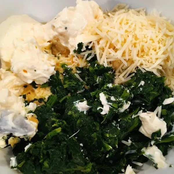 Spinach, garlic, chopped artichokes, Parmesan cheese and cream cheese in a large bowl ready to mix.