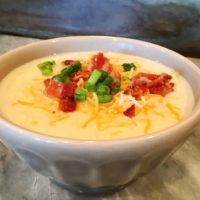 A bowl of potato soup with a cheese, bacon bits and chopped green onion on top