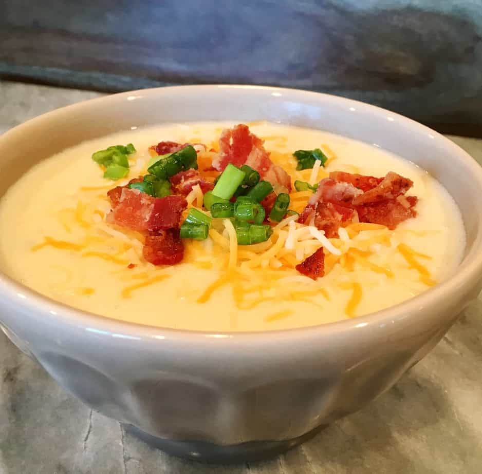 A bowl of potato soup with a cheese, bacon bits and chopped green onion on top