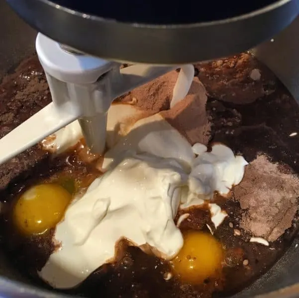 Mixer with chocolate cake mix, sour cream, eggs, and ingredients for Too Much Chocolate Cake