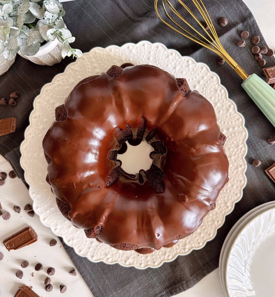 Overhead photo of Too Much Chocolate bundt cake on a white cake plate with a chocolate satin drizzle.