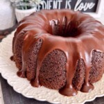 Side view of too much chocolate cake on a white cake plate.